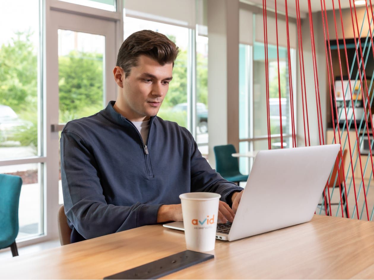 Homme travaillant sur son ordinateur portable assis à une table de petit-déjeuner avec un gobelet de café avid