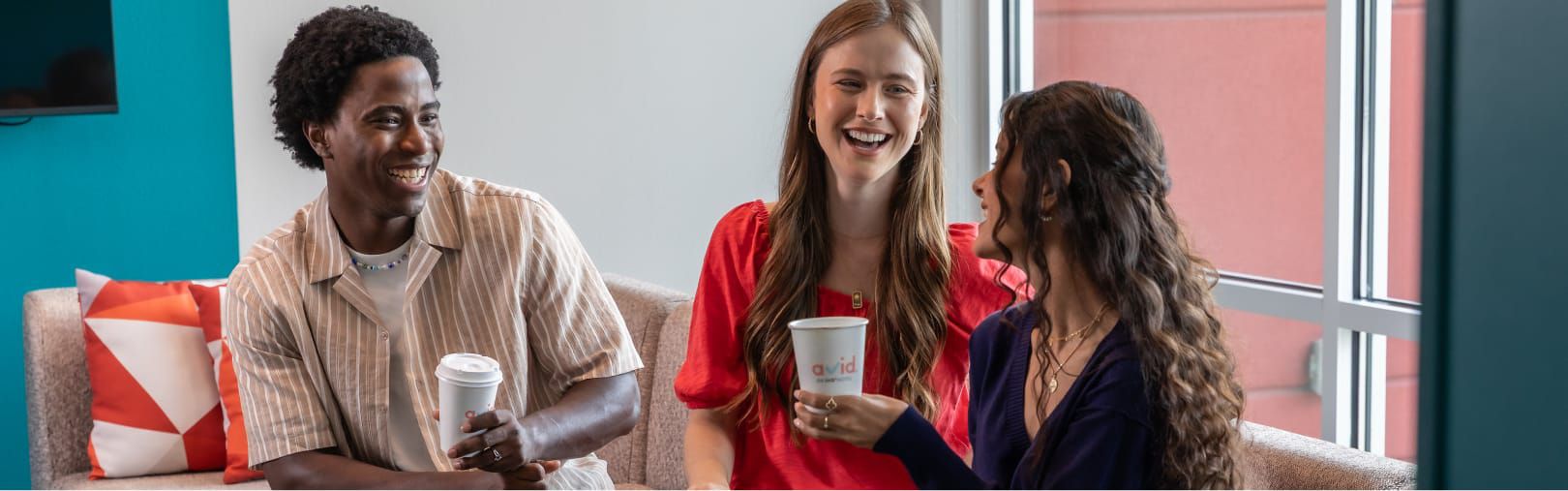 Trois amis assis sur un canapé buvant du café dans des gobelets avid à emporter