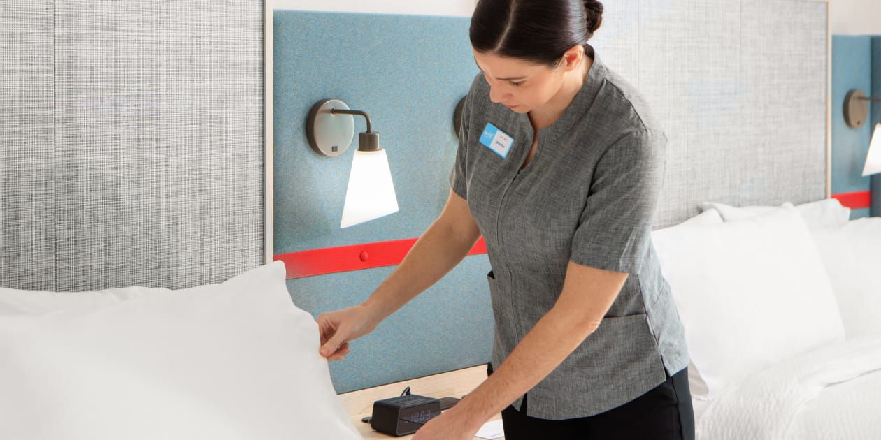 Housekeeper straightening pillow on freshly made bed