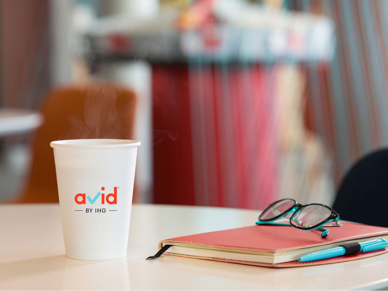 Coffee cup with avid logo, notebook, and glasses lying on table