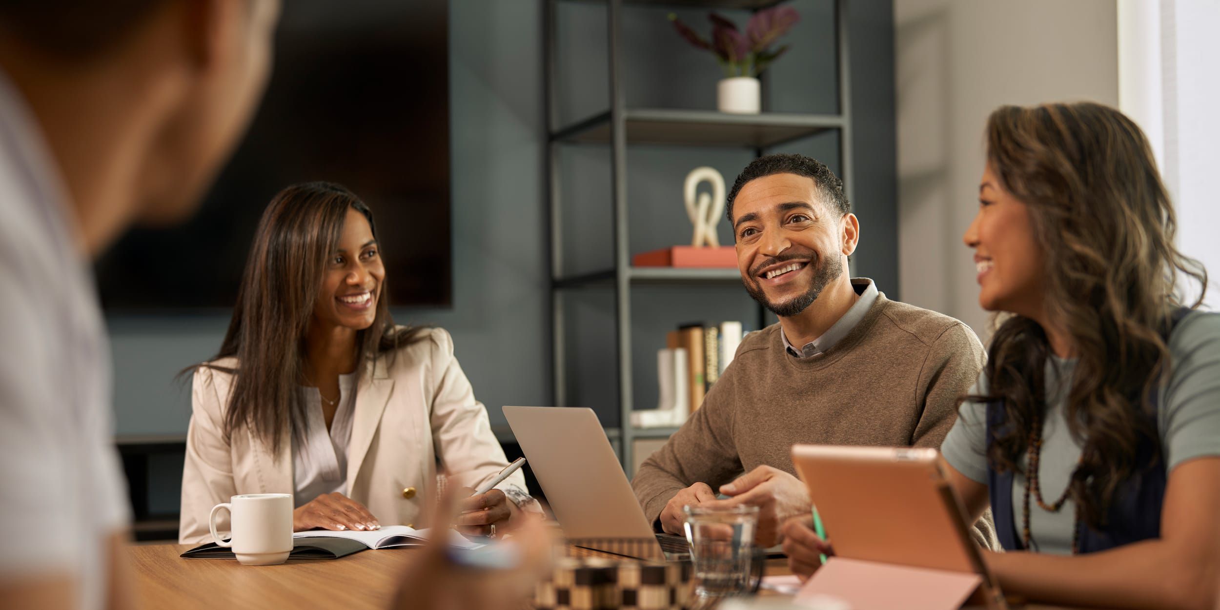 Coworkers smiling and talking around a table with laptops.
