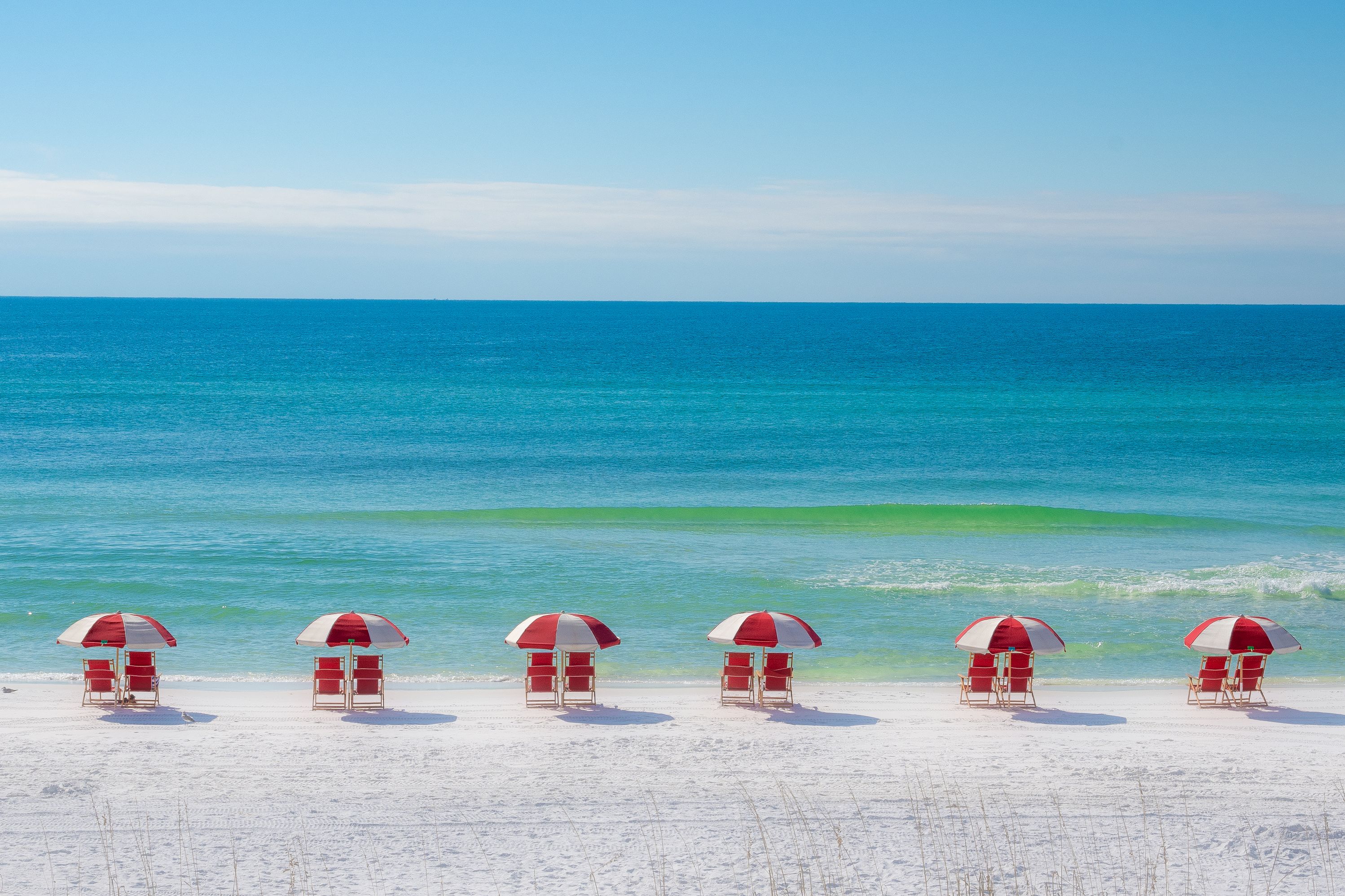 Red beach chairs and umbrellas on shore in front of ocean.