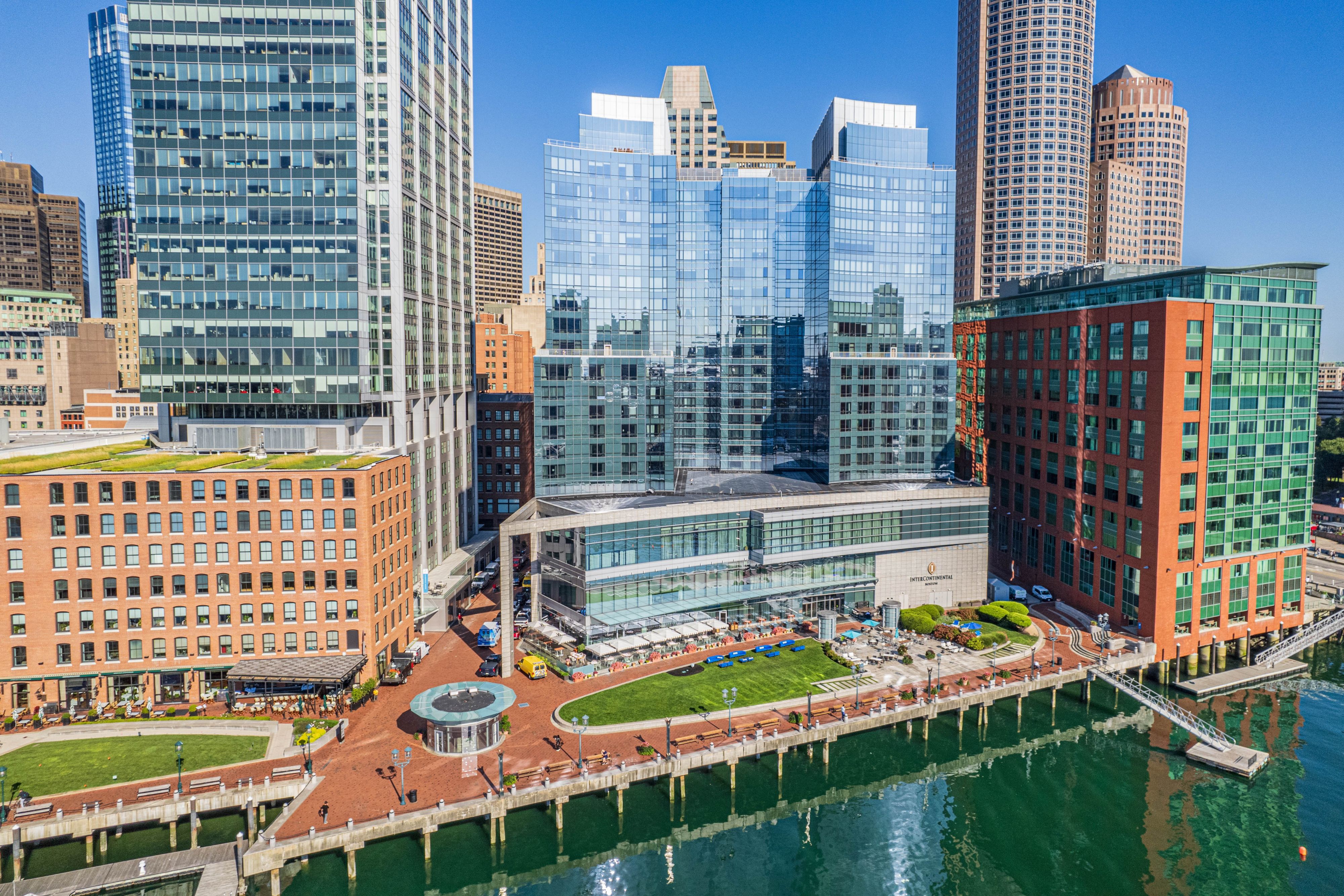 Aerial view of InterContinental Boston along Boston Harbor, showcasing the waterfront promenade, outdoor terrace, marina access, and surrounding downtown skyline on a clear day.