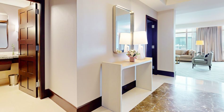 Suite foyer with elegant furnishings, adjacent bathroom, and a bright living area beyond.