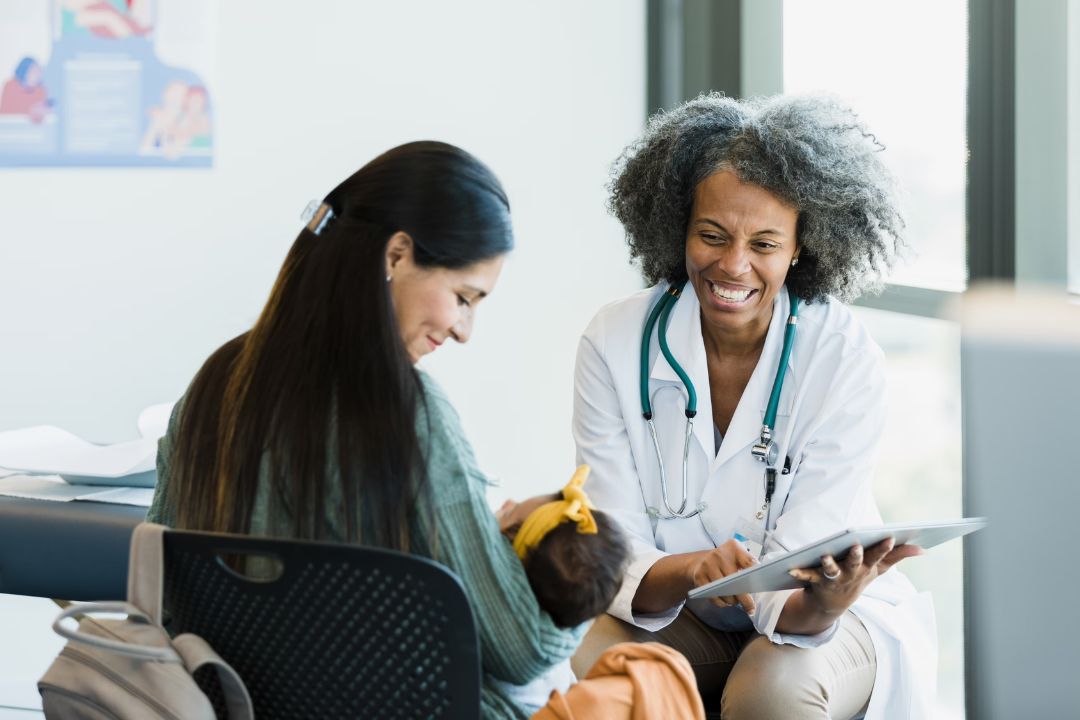 Doctor speaking with a new mom and her baby in a medical office.