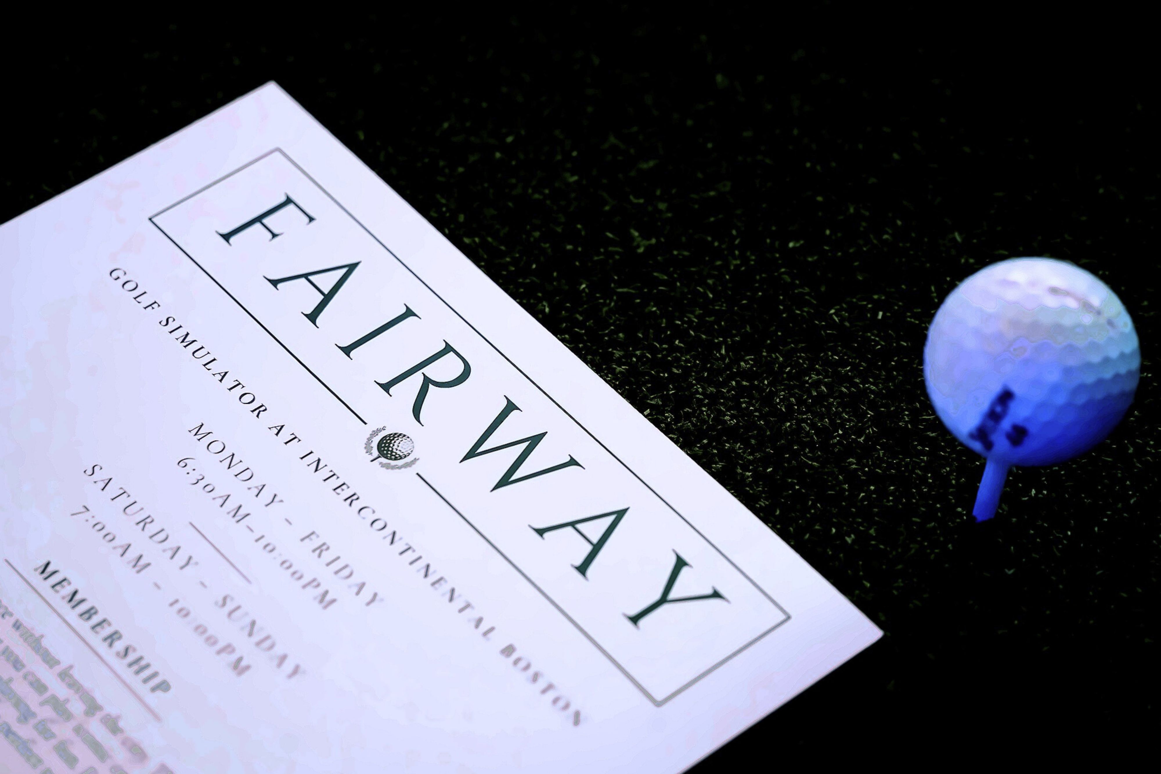 A FAIRWAY golf simulator brochure lying on turf next to a golf ball on a tee.