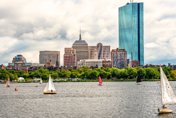Boston Harbor with sailboats spread throughout and views of Boston buildings.