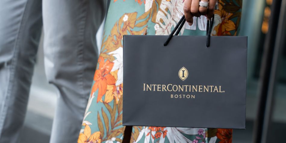Hand holding black InterContinental Boston gift bag with gold logo.
