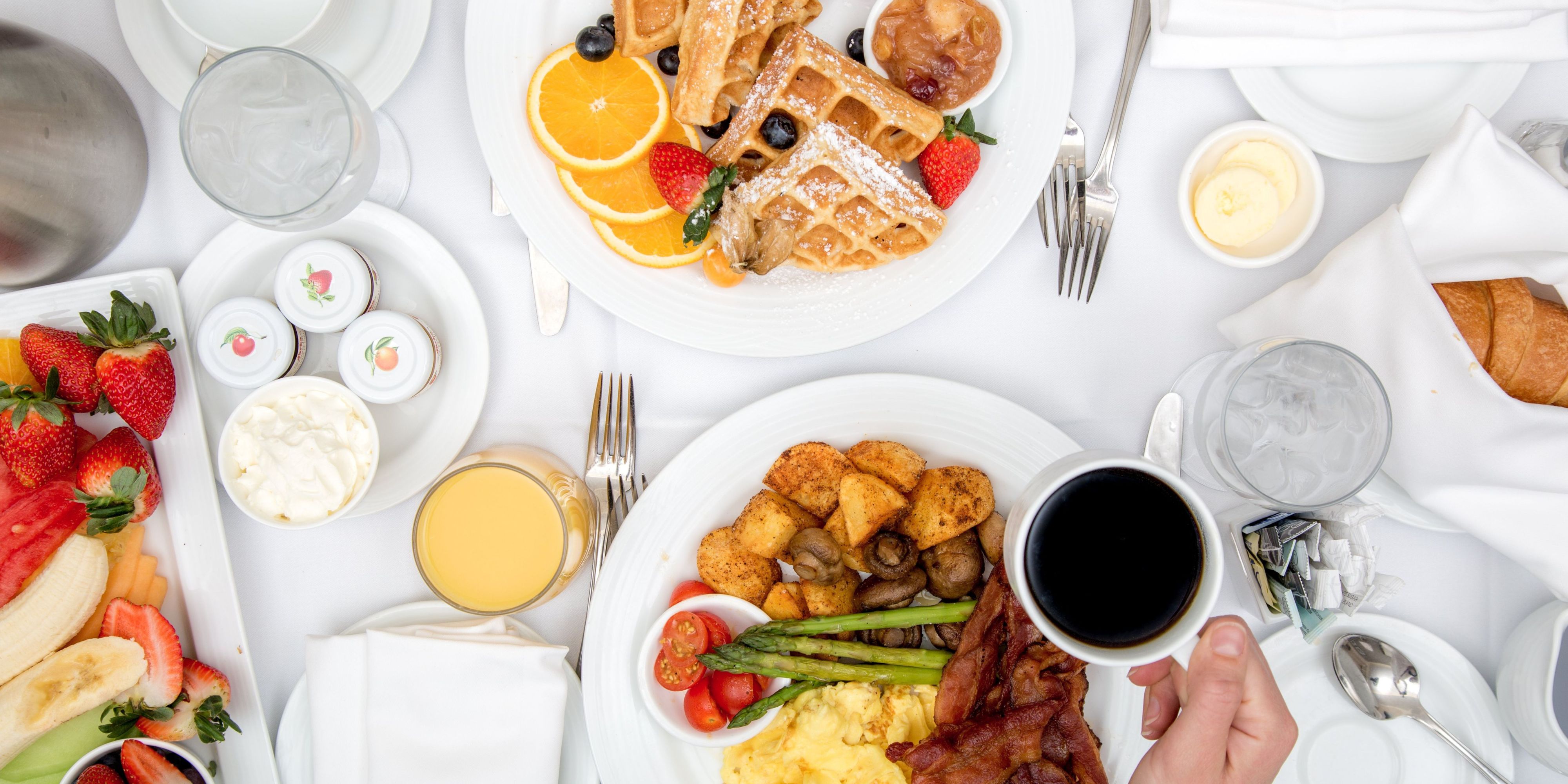 Assortment of breakfast dishes from the in-room dining menu, including waffles, eggs, potatoes, bacon, fruit, bread, coffee, juice, and accompaniments.