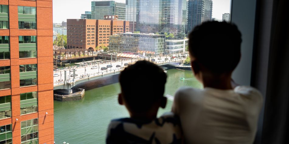 Kids gaze at the Boston harbor and skyline from a hotel window.