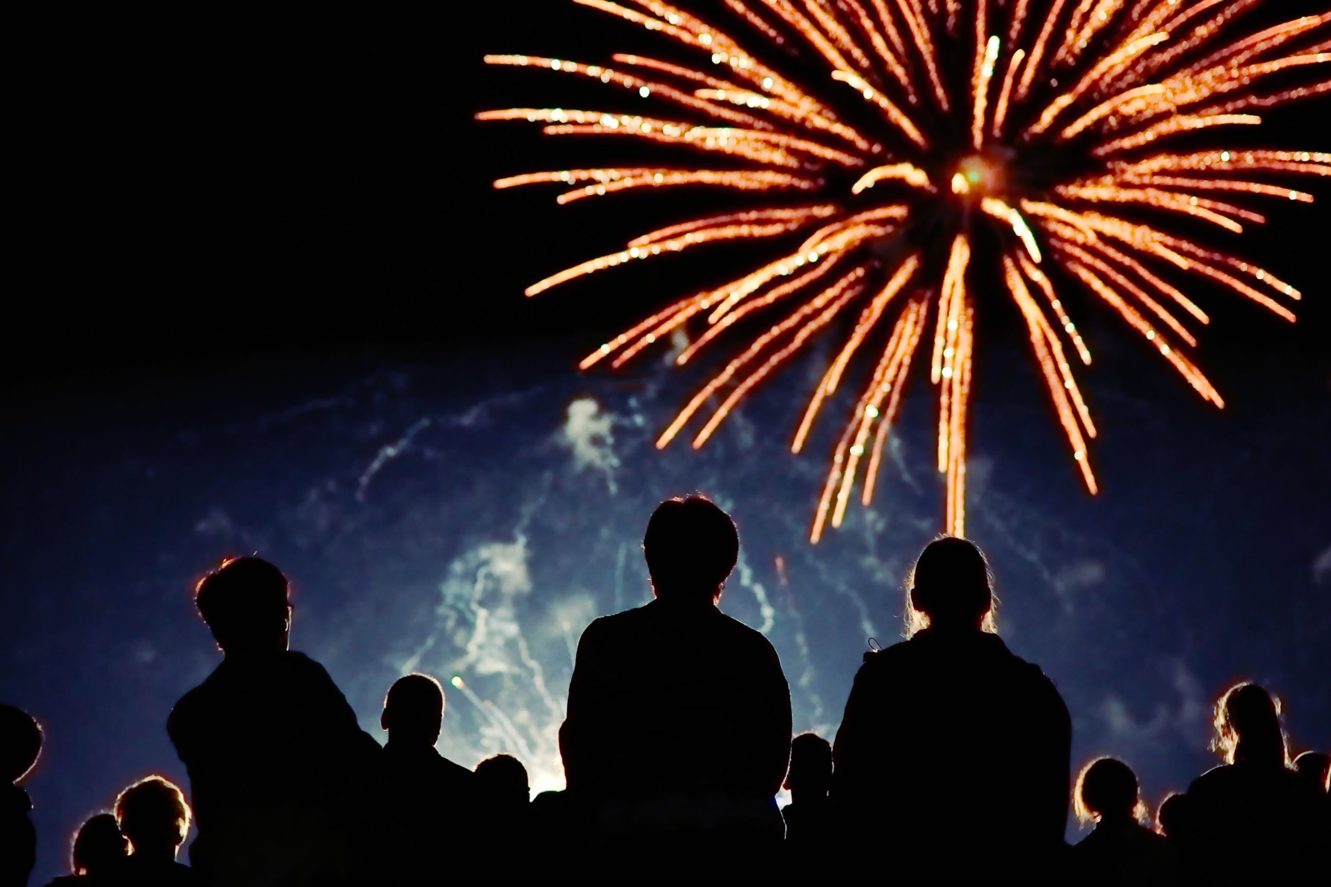 Guests gather outdoors at night to watch colorful fireworks burst across the sky.