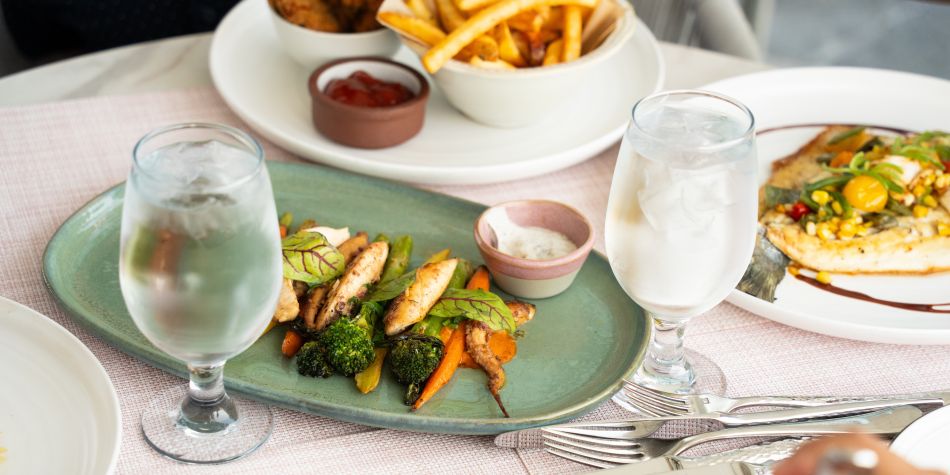 Freshly prepared lunch spread at InterContinental Boston featuring grilled chicken with seasonal vegetables and herb dip, artisan flatbread, crispy fries, and chilled water served on an elegant dining table.