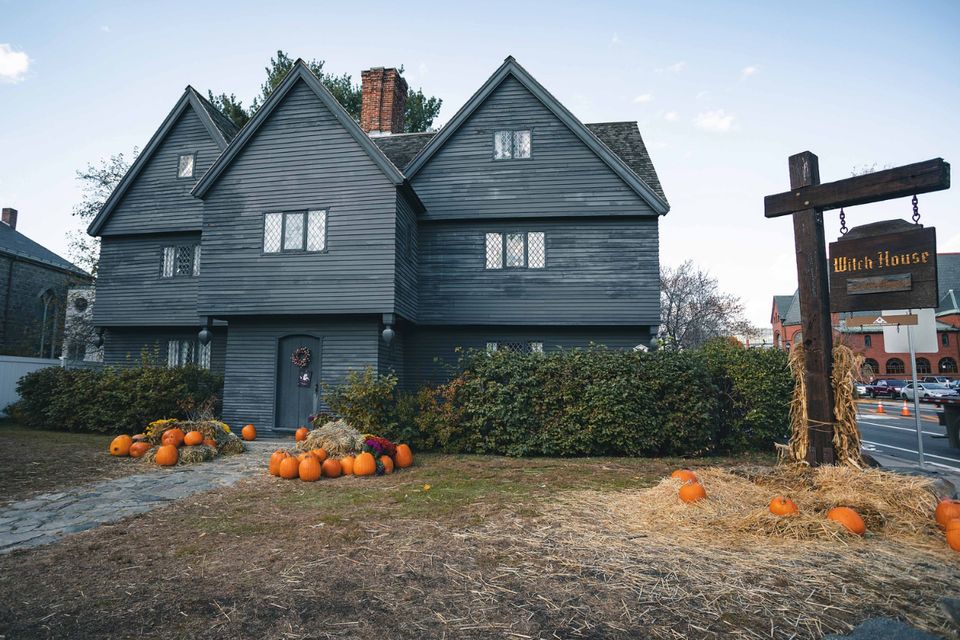Black house with 'Witch House' sign and pumpkins out front. 