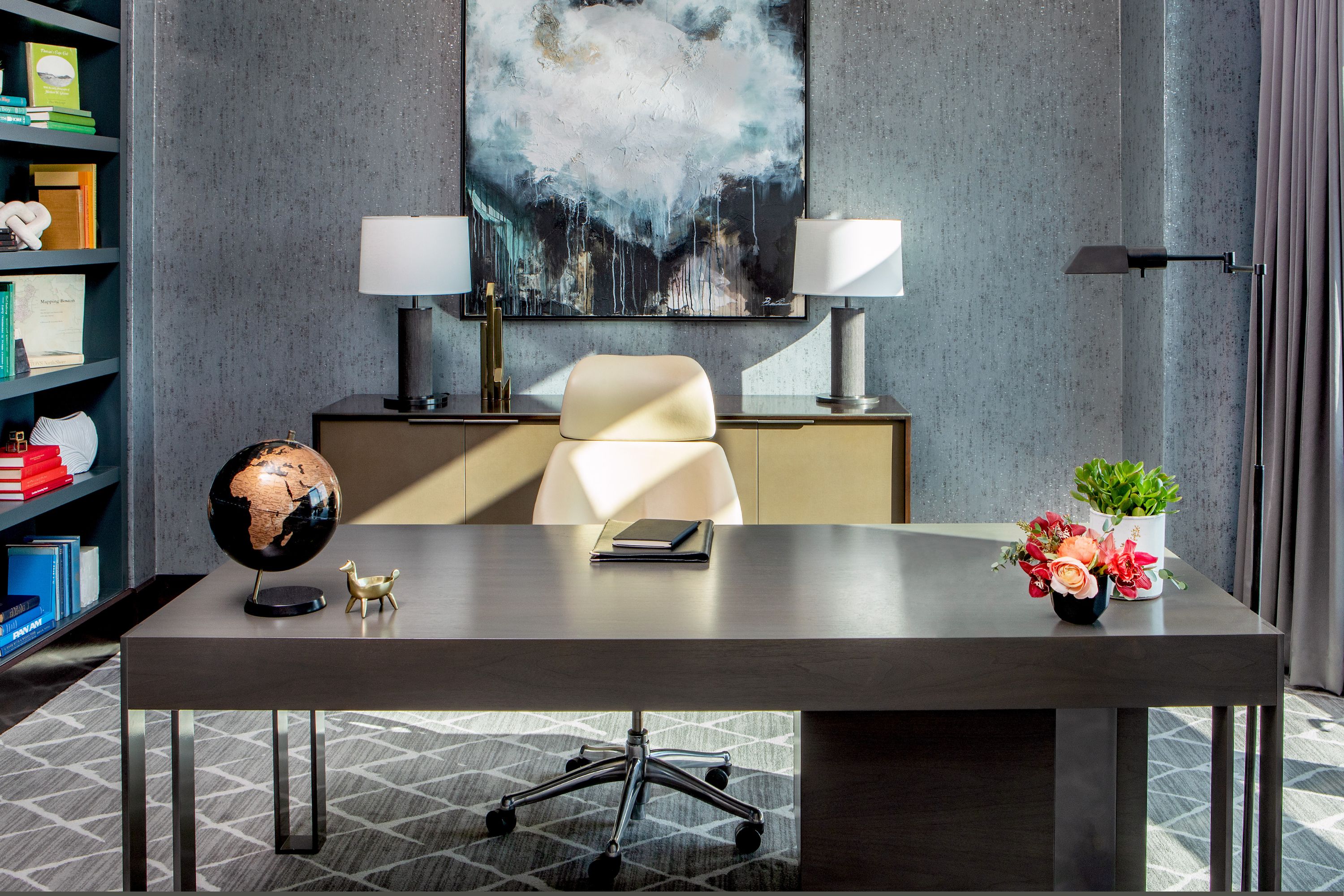 Modern suite workspace with a desk, chair, bookshelf, and abstract artwork, styled with table lamps and decorative accents.