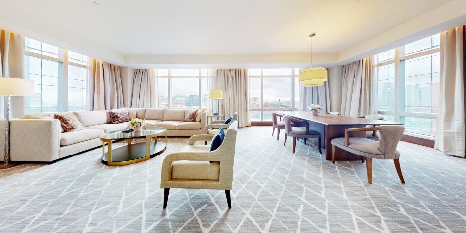 Open-concept living and dining space with sectional sofa, armchairs, coffee table, and dining area framed by large windows.