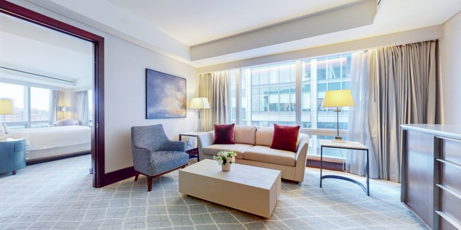 Separate sitting area with a sofa, armchair, and coffee table, overlooking city views through wide windows.