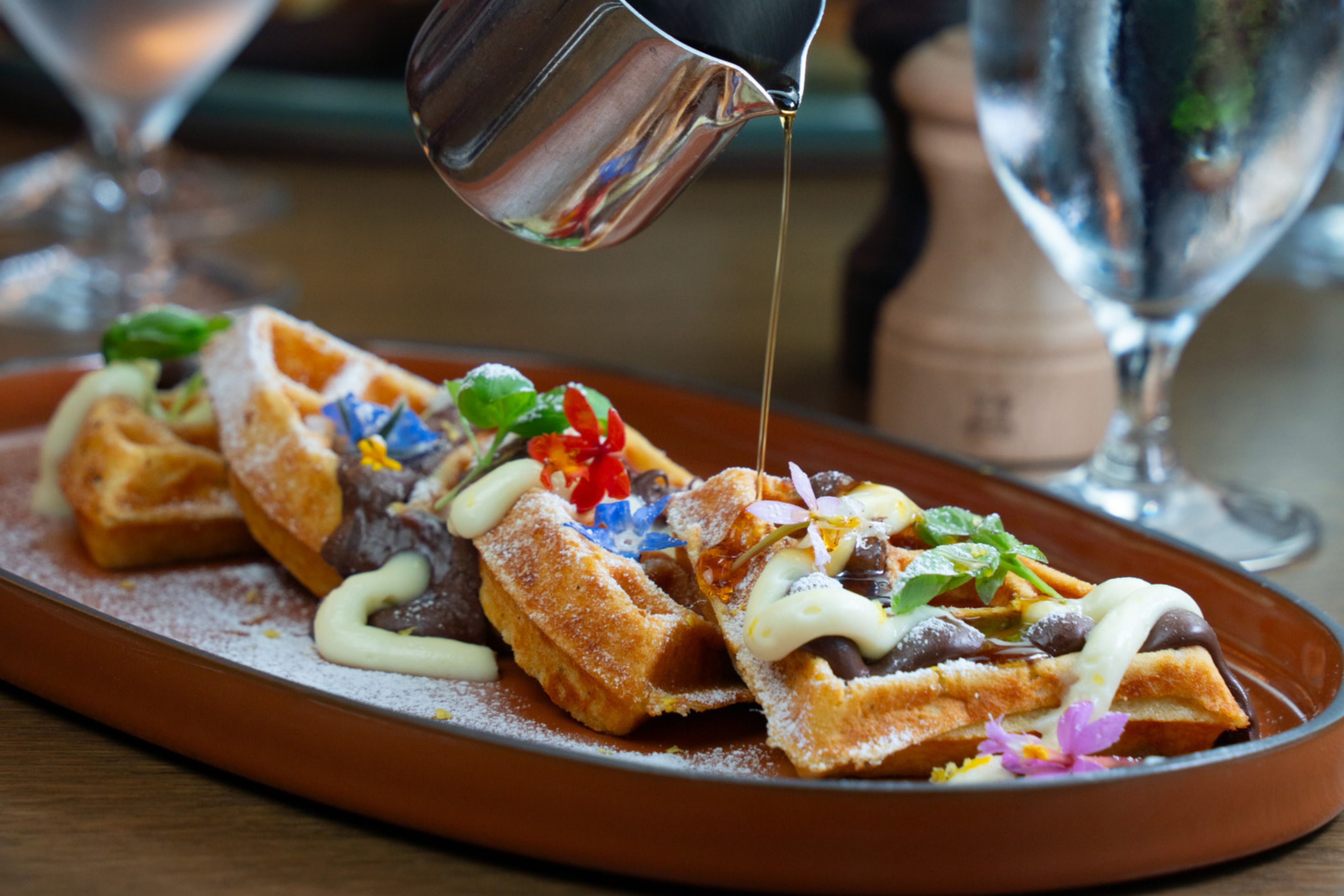Artfully plated waffles drizzled with syrup and edible flowers.