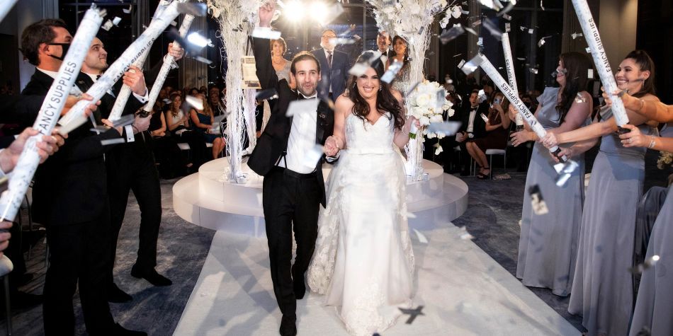Couple walking down the aisle surrounded by guests with confetti poppers.