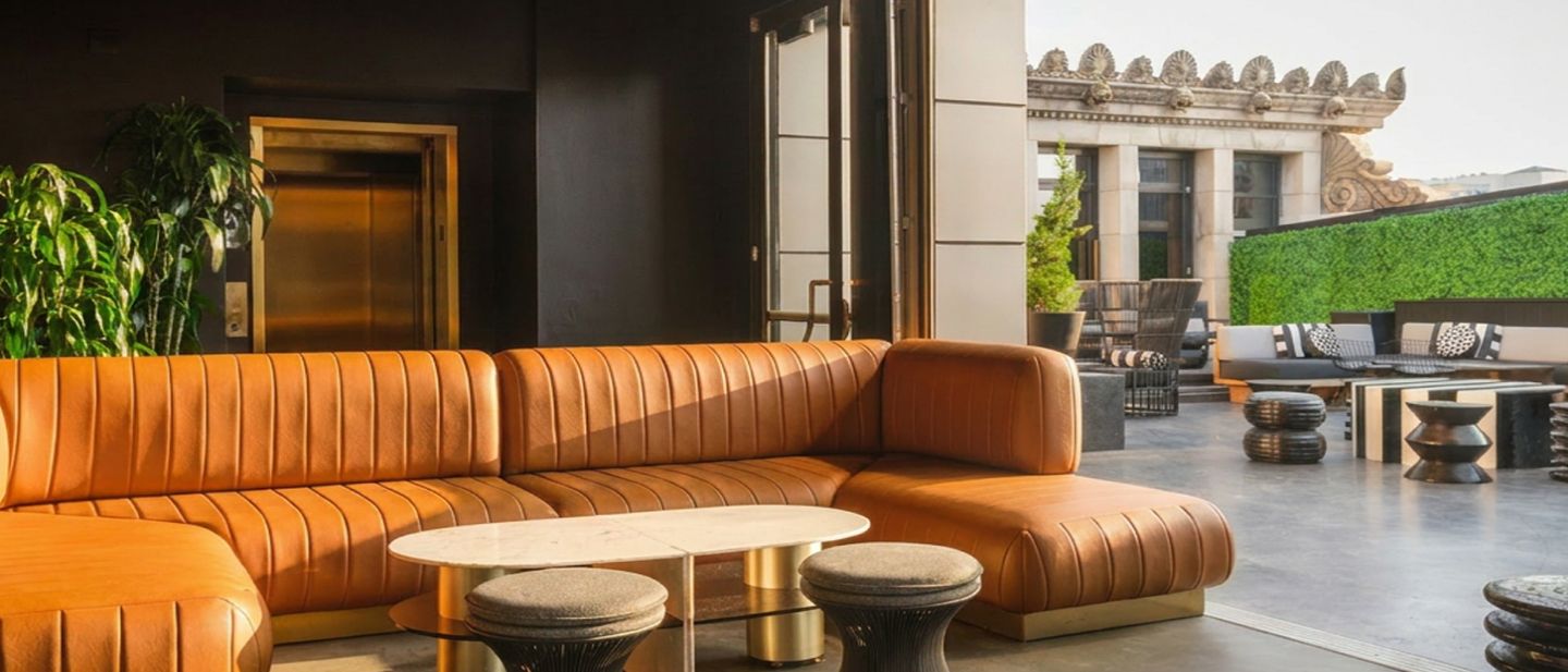 A lounge with a curved orange leather sofa, natural light, and indoor plants.
