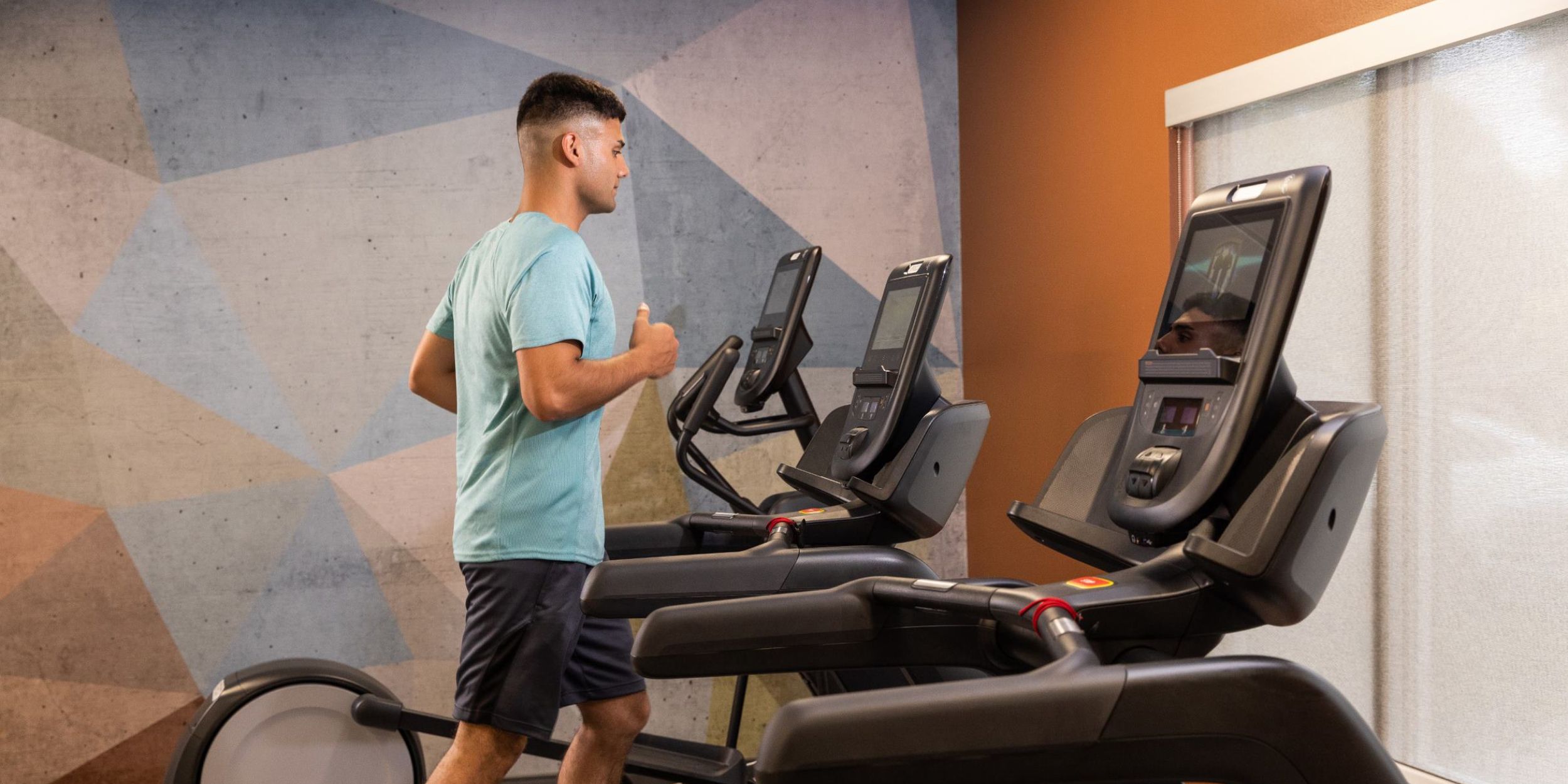 A guest running on a treadmill in atheltic wear surrounded by other exercise equipment in the hotel gym