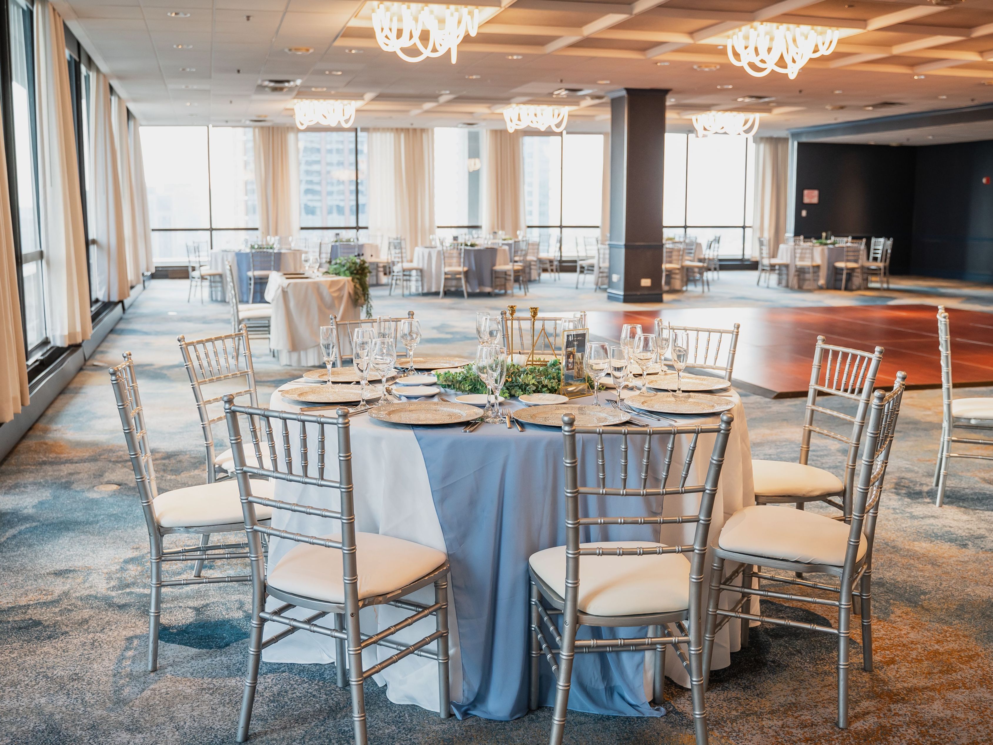 Ballroom with round tables, a dance floor, and table set for the bride and groom