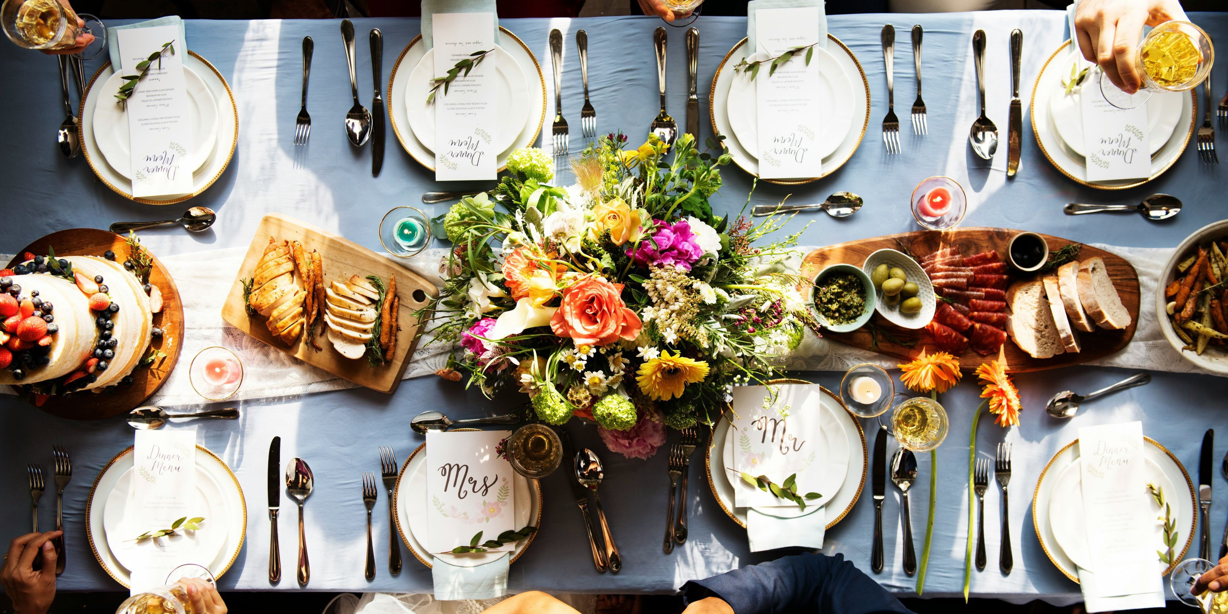 Overhead view of a long table with place settings, shared dishes, and a floral centerpiece.