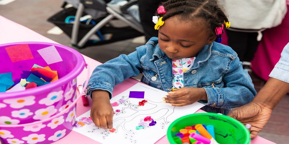 Child creating a colorful art project with tissue paper and markers at a craft table.