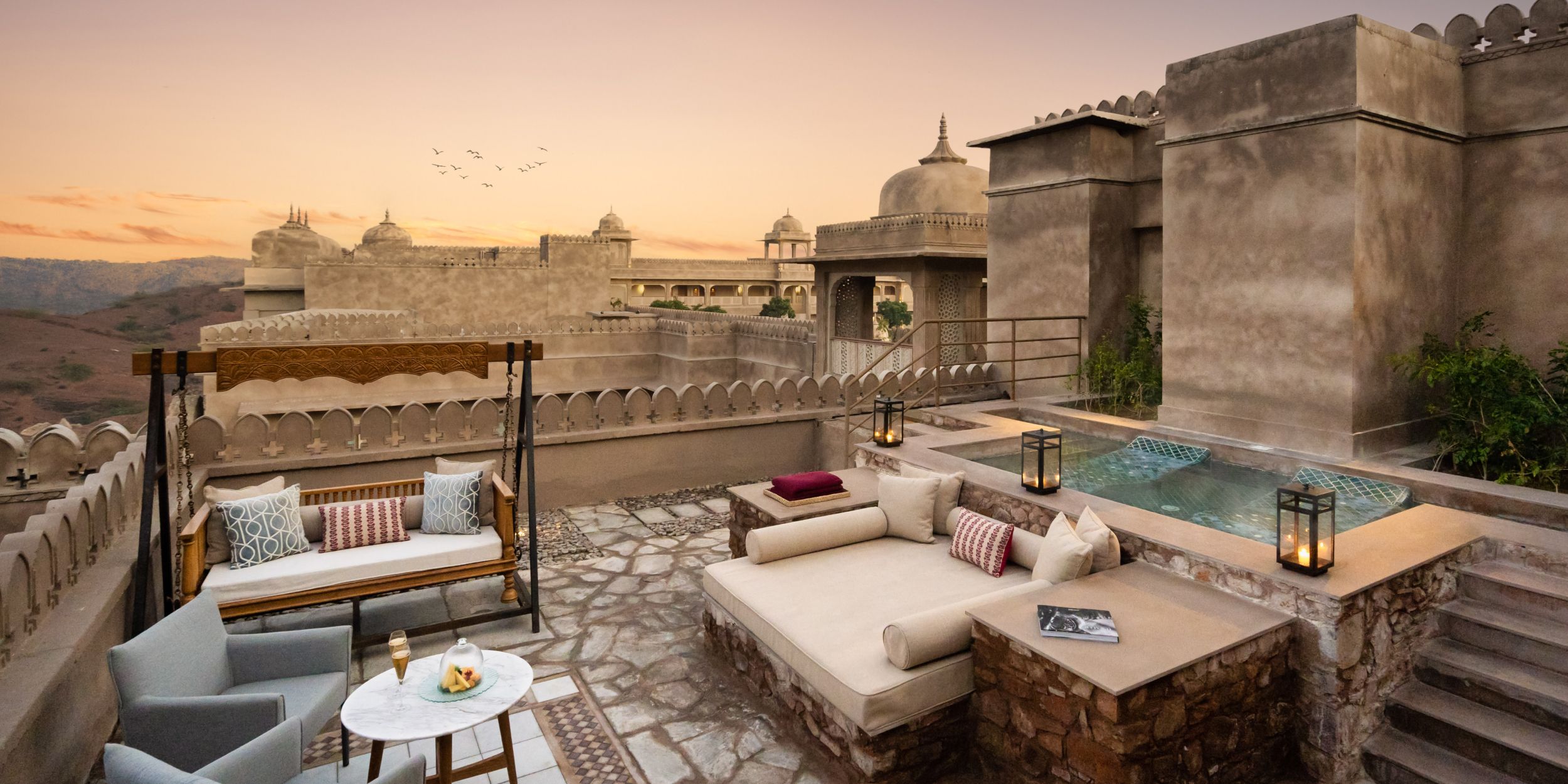 Luxury rooftop terrace with lounge seating, lanterns, and a plunge pool overlooking historic architecture at sunset. 