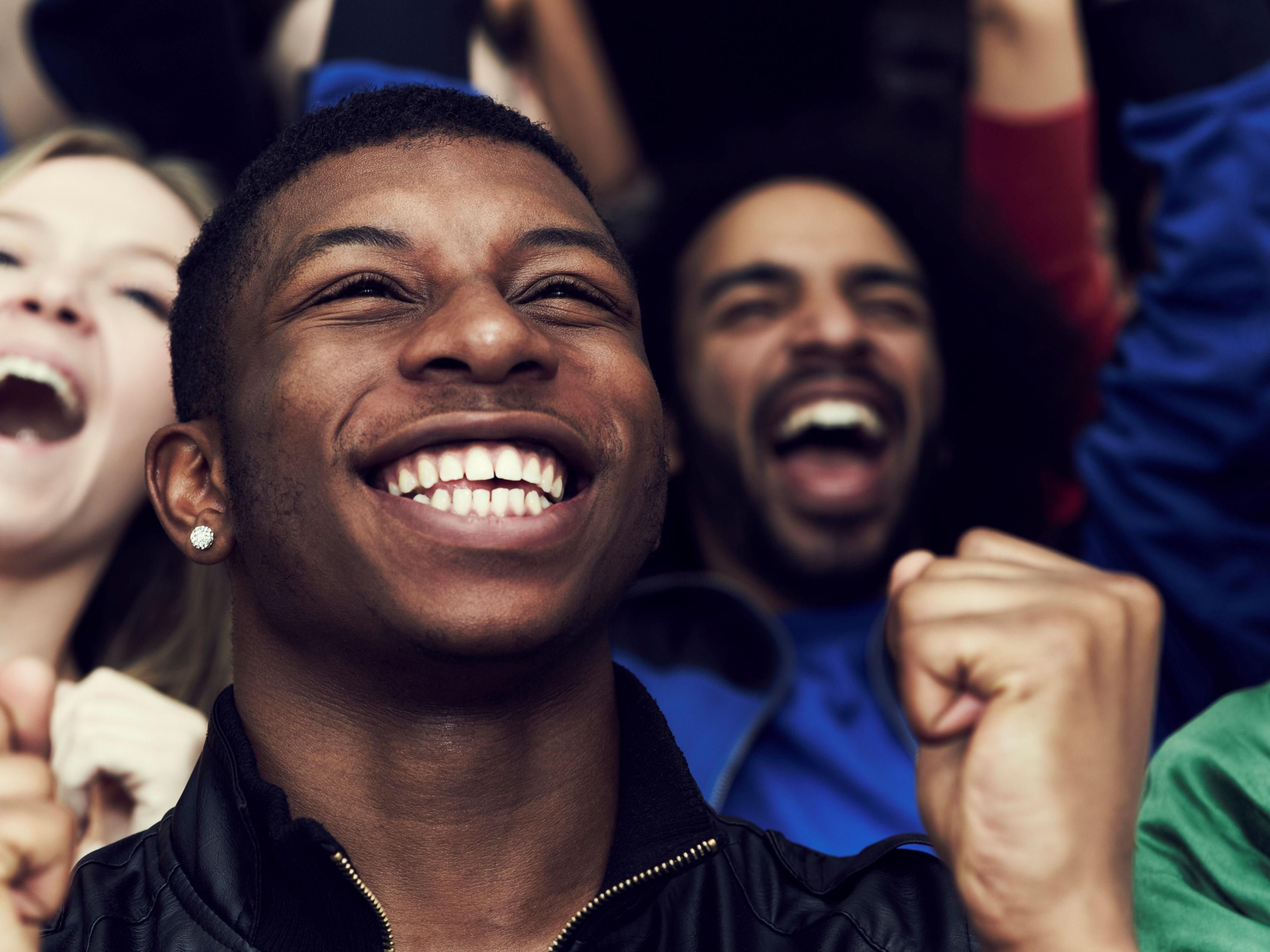Man sitting in a sports game crowed smiling with excited fans behind him