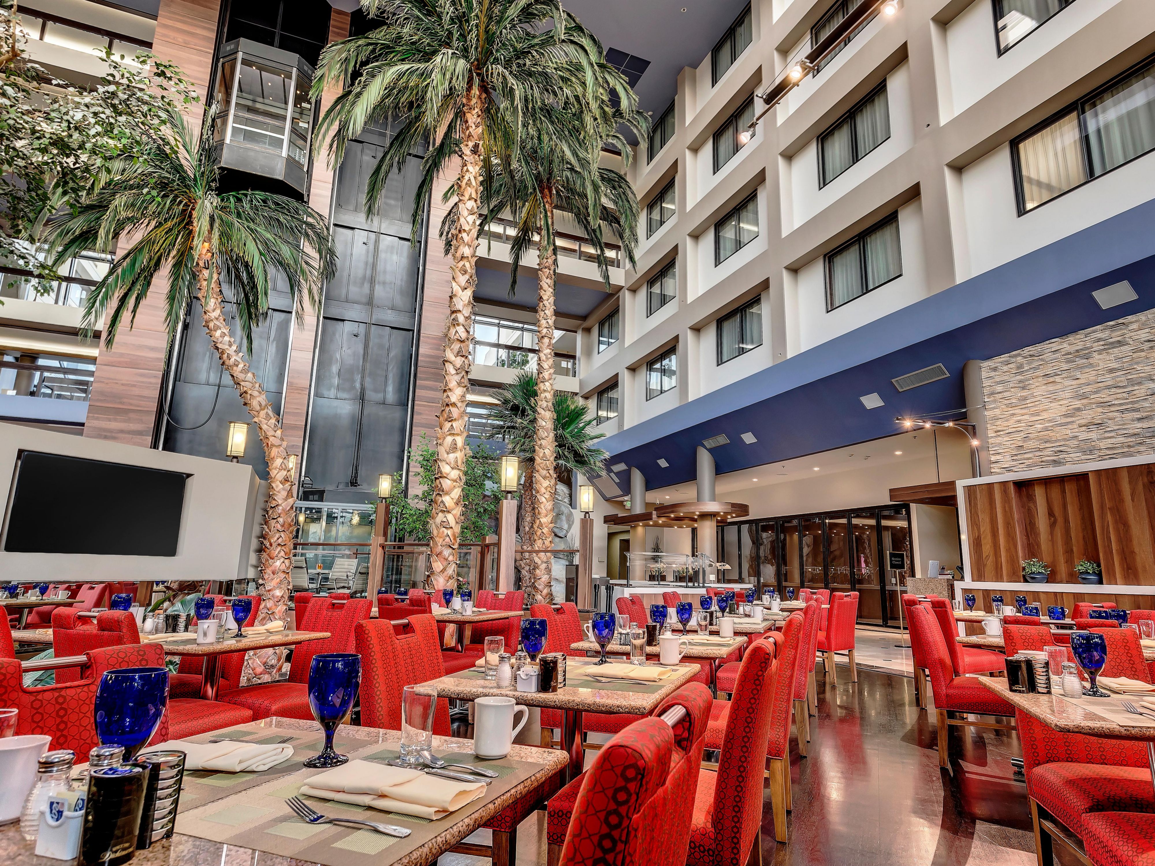 Atrium dining area with palm trees and red cushioned chairs.