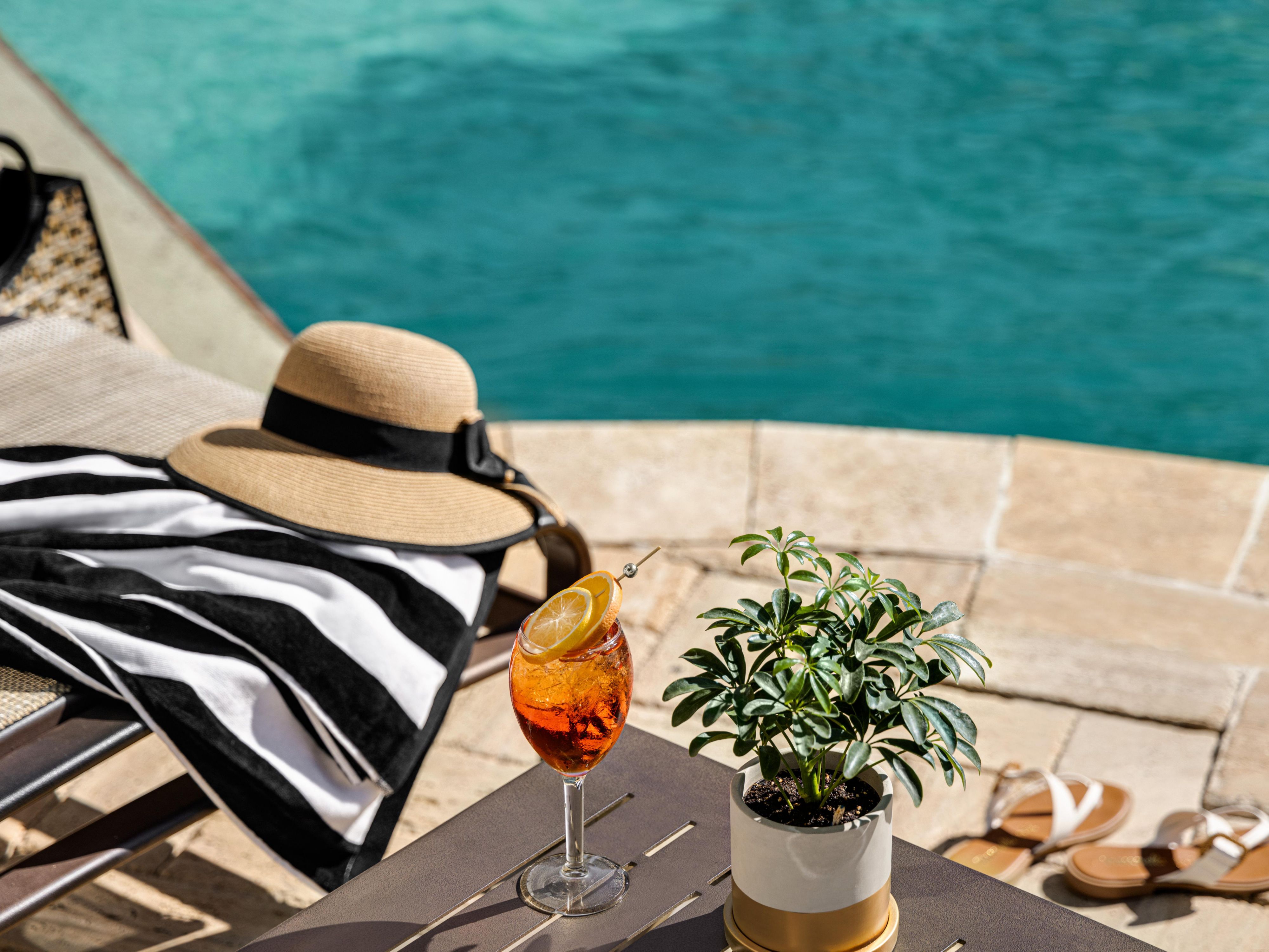 cocktail, sun hat and towel by the pool
