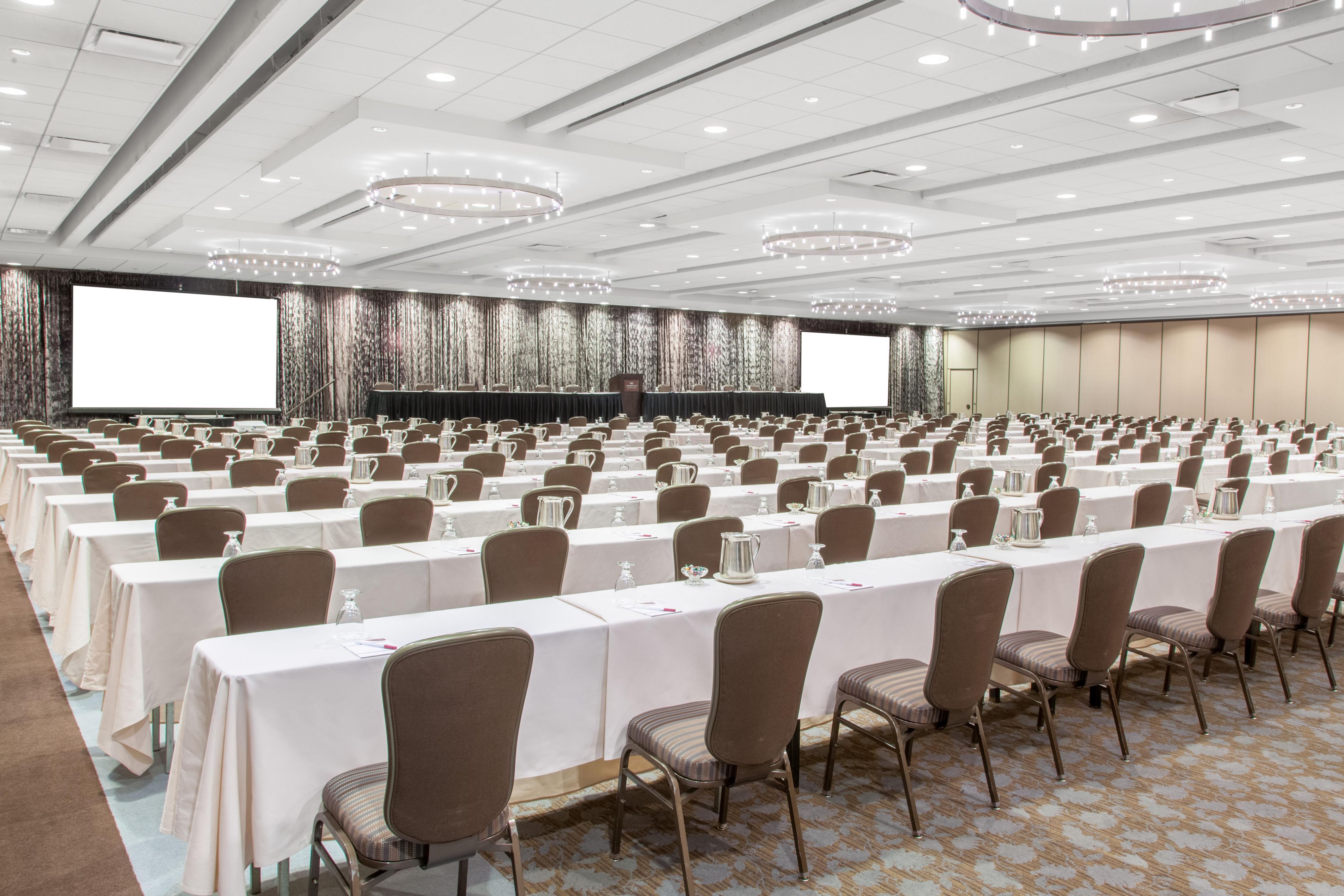 Meeting space that can accommodate a large group with long tables and white linens