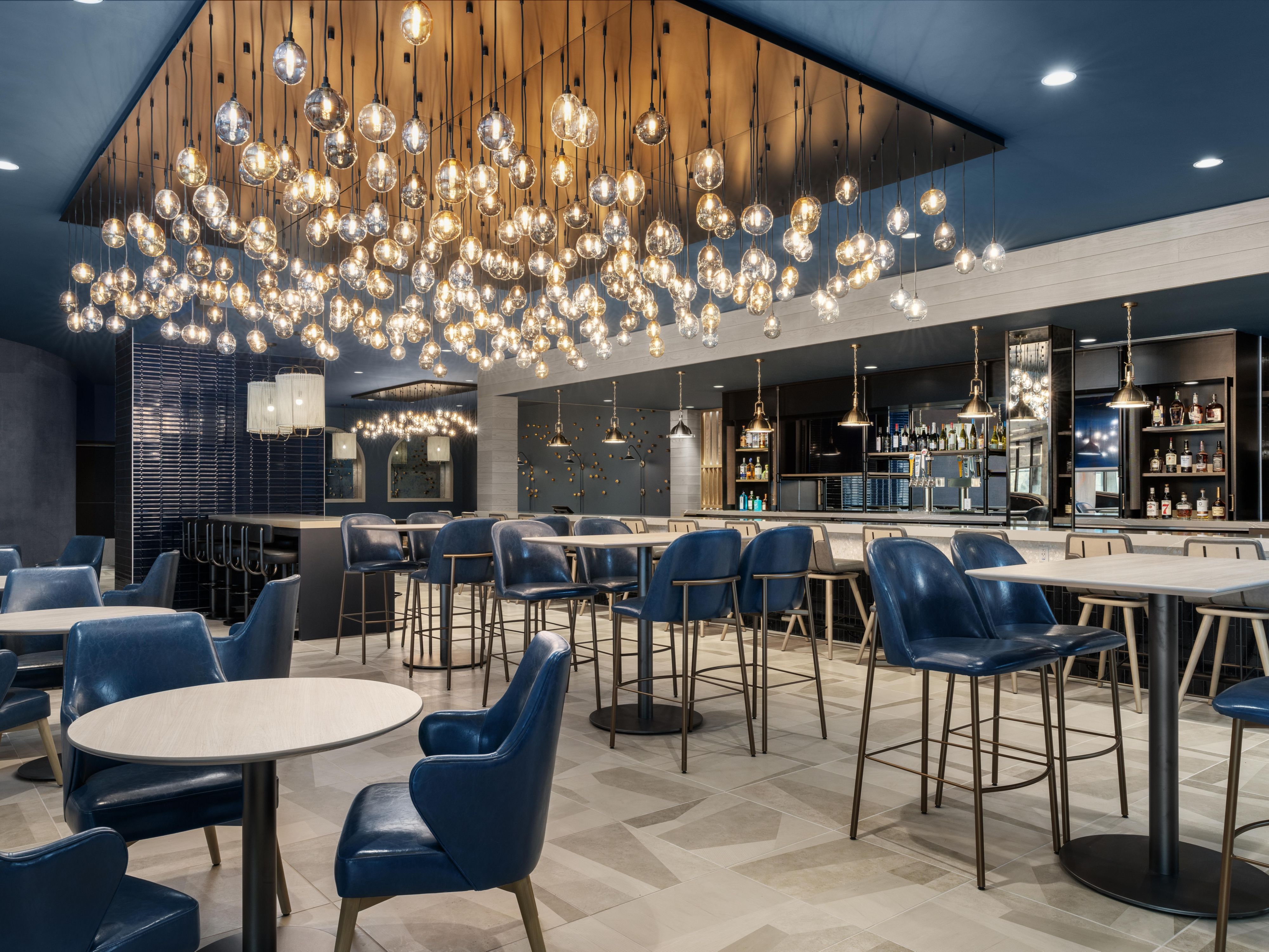 Dining room of Tines Restaurant t with chandelier and backlit bar.