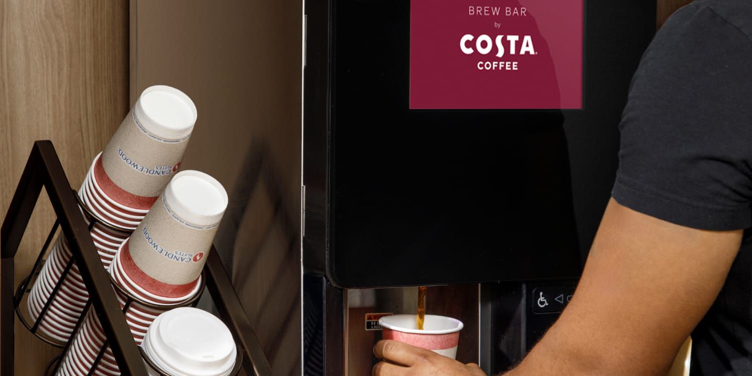 A person getting coffee at a coffee machine with Costa logo on the screen