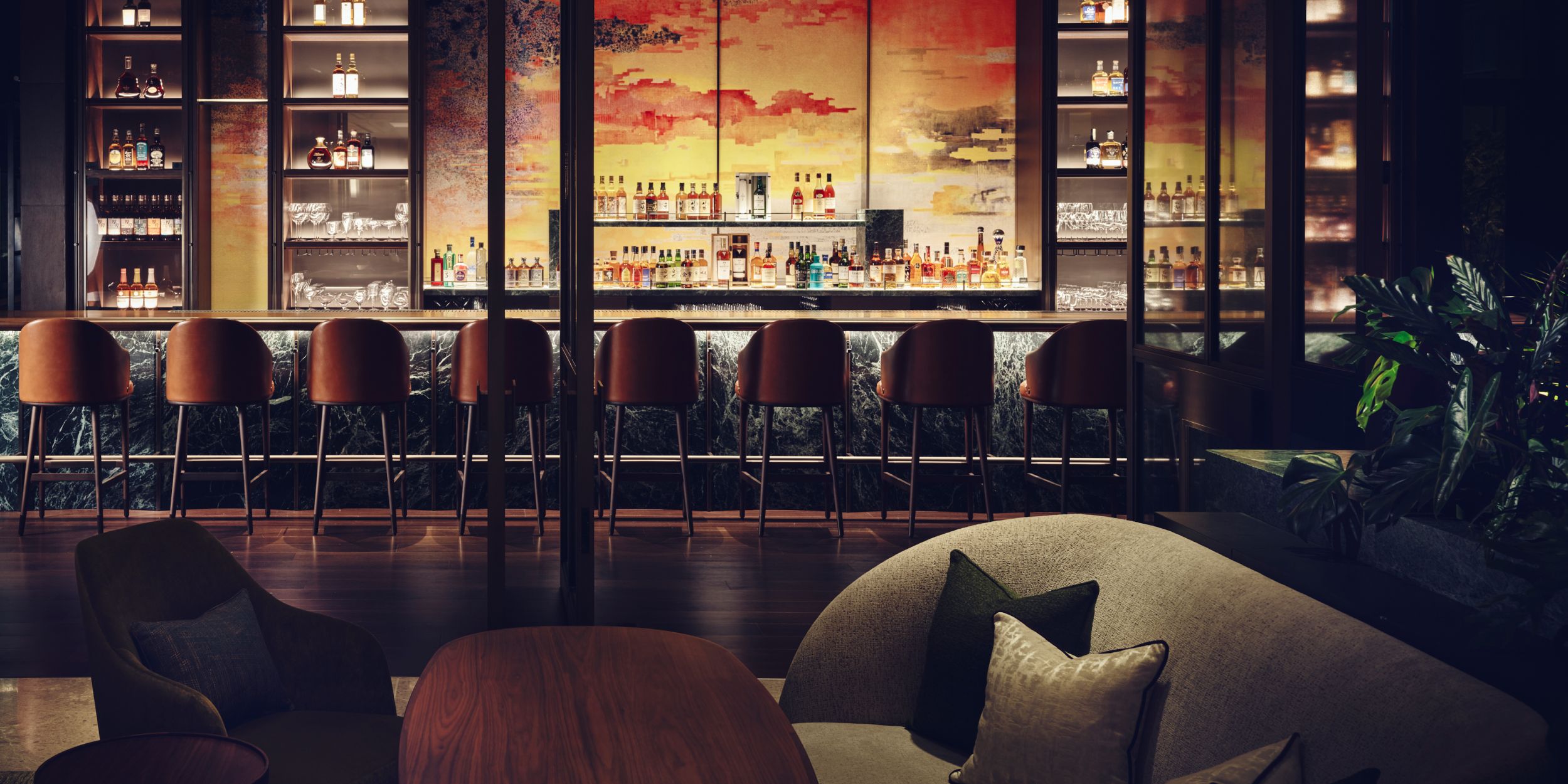 A fully stocked bar with a vibrant mural of reds, oranges, and yellows as a backdrop.