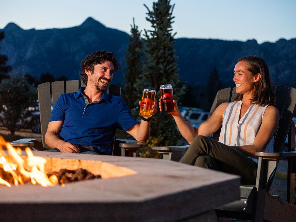 Couple cheers with beer by a firepit