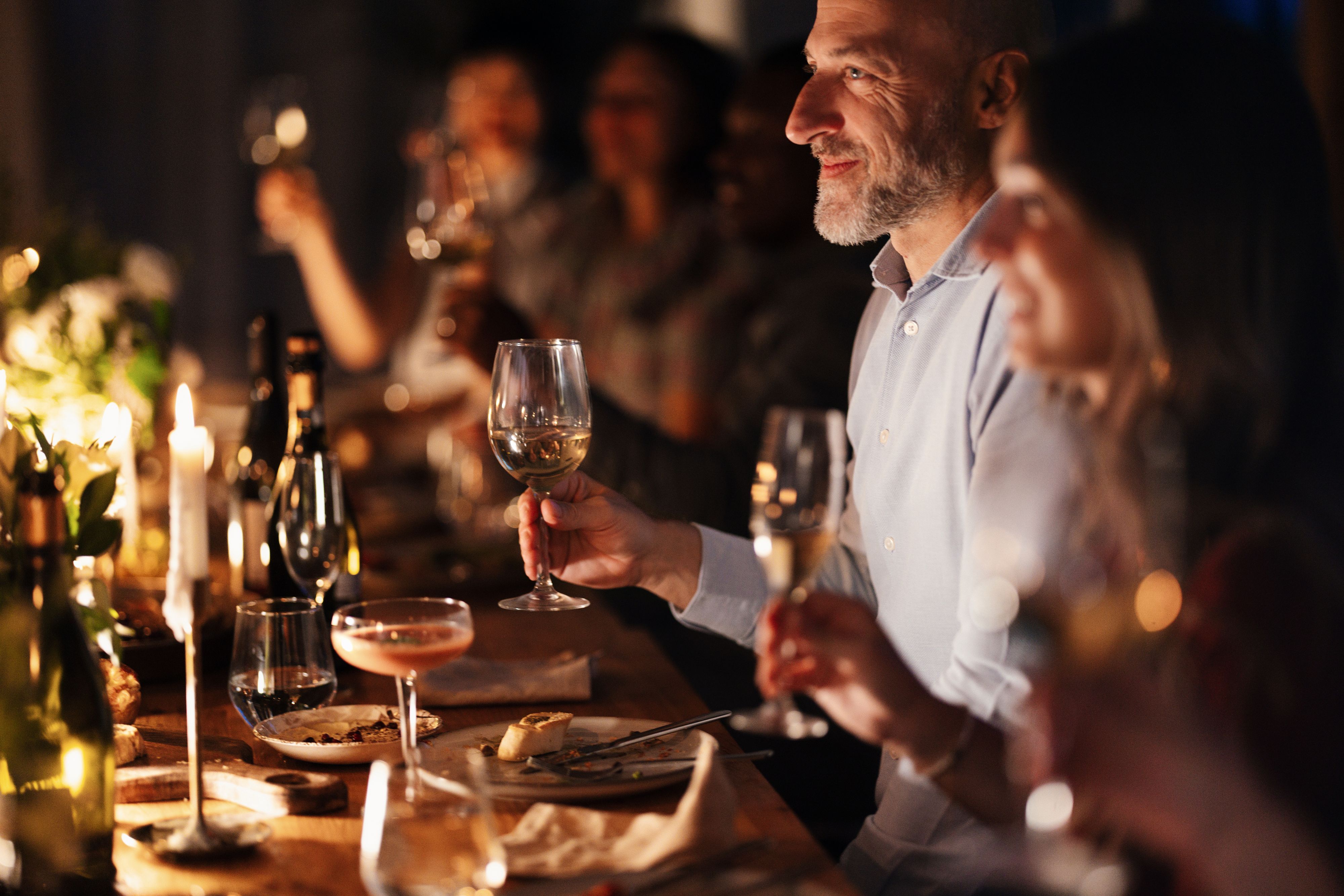 Huéspedes cenando juntos a la luz de las velas con vino y cócteles.