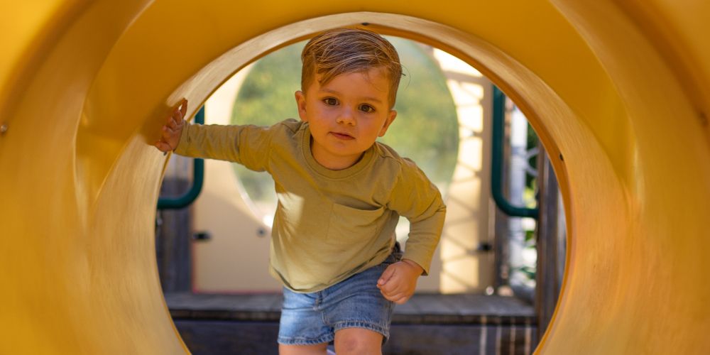 Child playing on playground climbing through tube