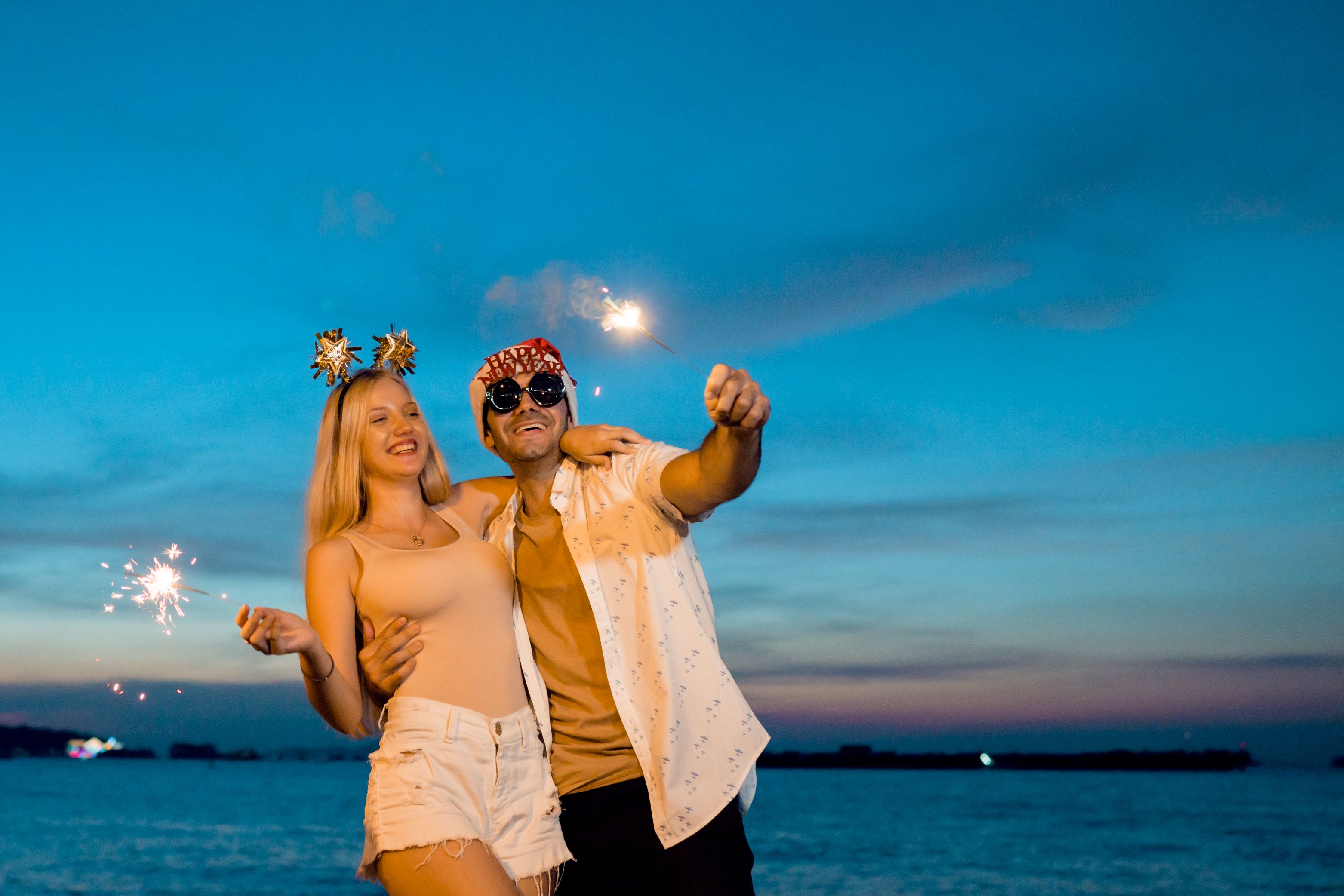 Two people hold sparklers by the water during a New Year’s celebration.