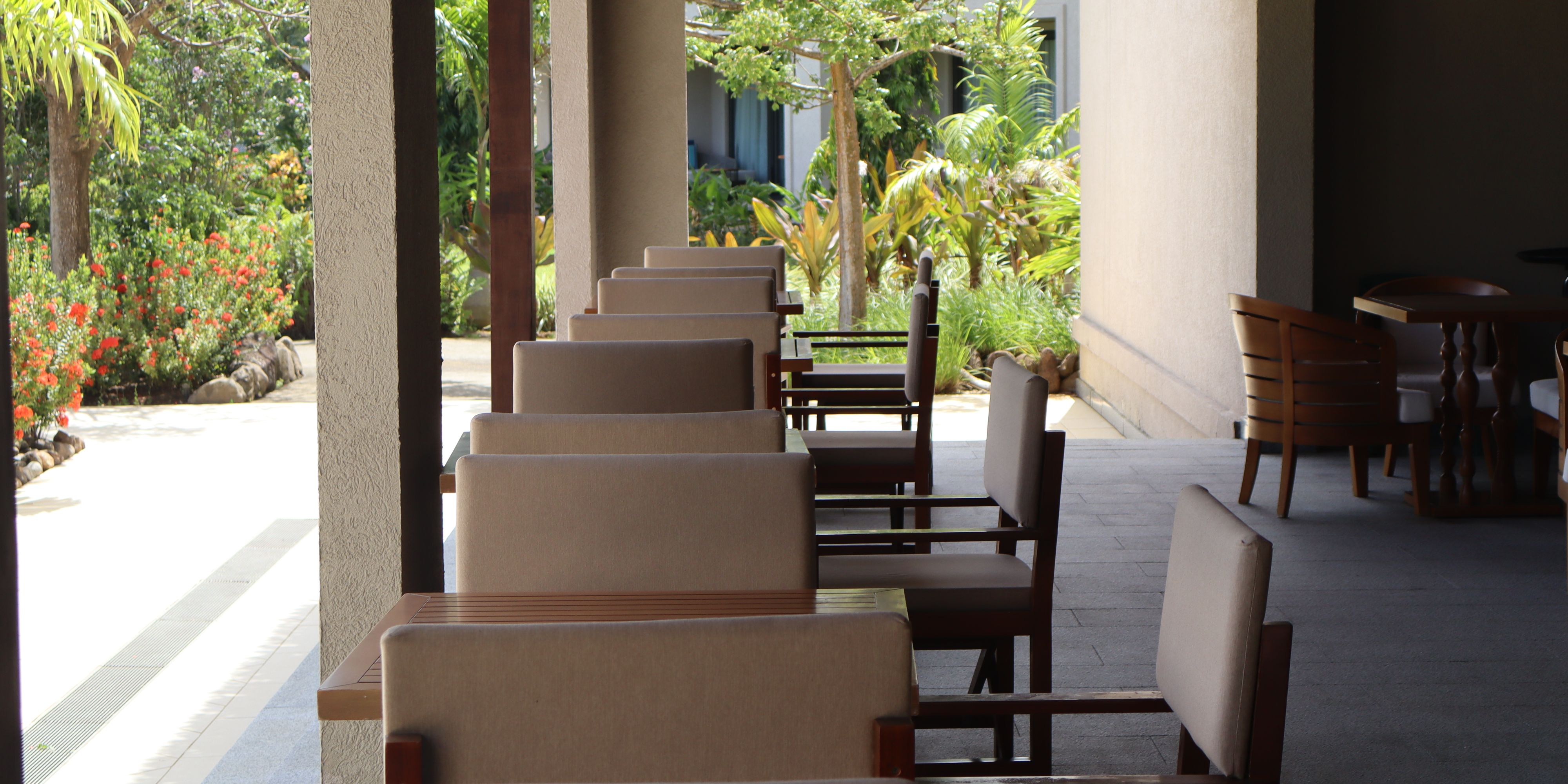 Covered outdoor seating at Saltwood restaurant overlooking tropical gardens, with comfortable lounge-style chairs and shaded tables for open-air dining.
