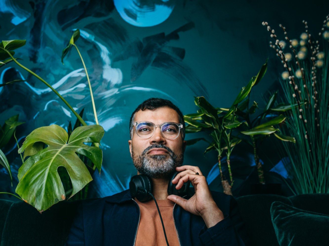 Man with headphones sitting in a room with a lot of plants