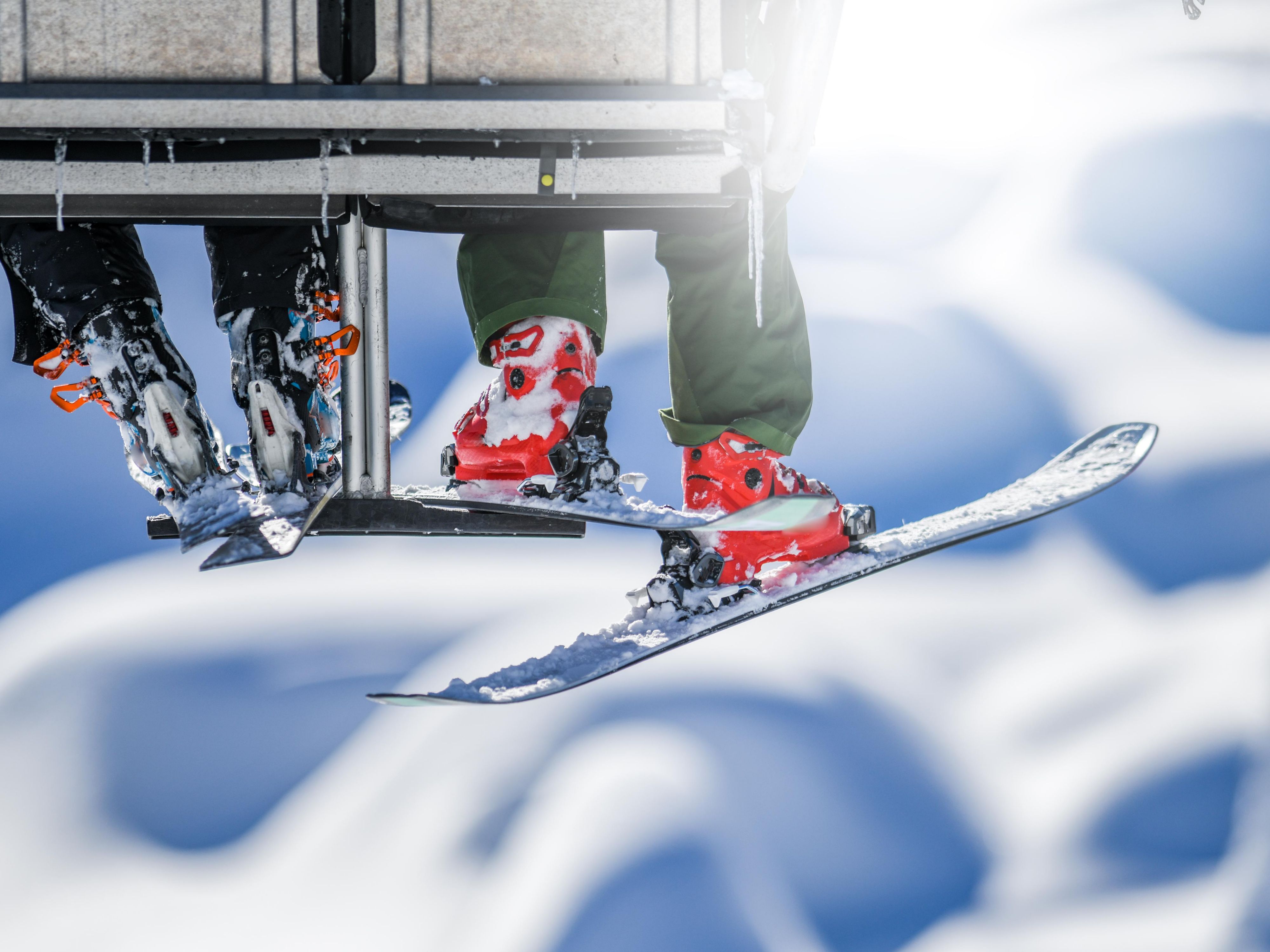 Skis and feet hanging off of a snowlift with snowbanks in the background