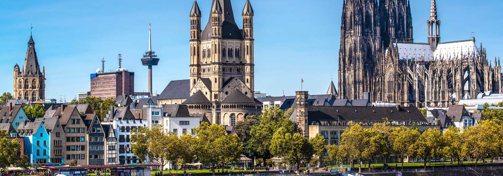 view of Cologne cathedral with green trees in the foreground and bright blue sky above 