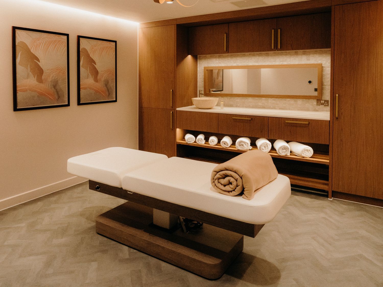 luxury spa treatment room with a massage table, flower wall prints and a sink