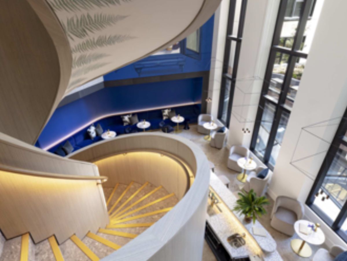 Modern hotel bar with curved staircase and lounge seating.