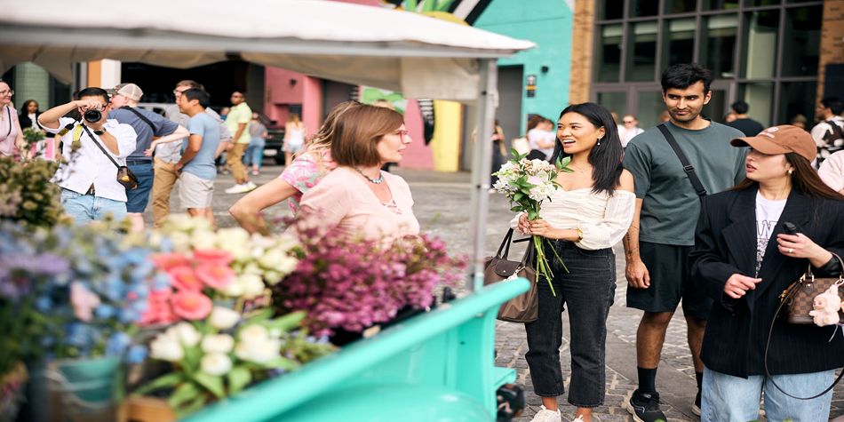 People browsing a street flower market, including a person holding a bouquet while others look at floral displays.