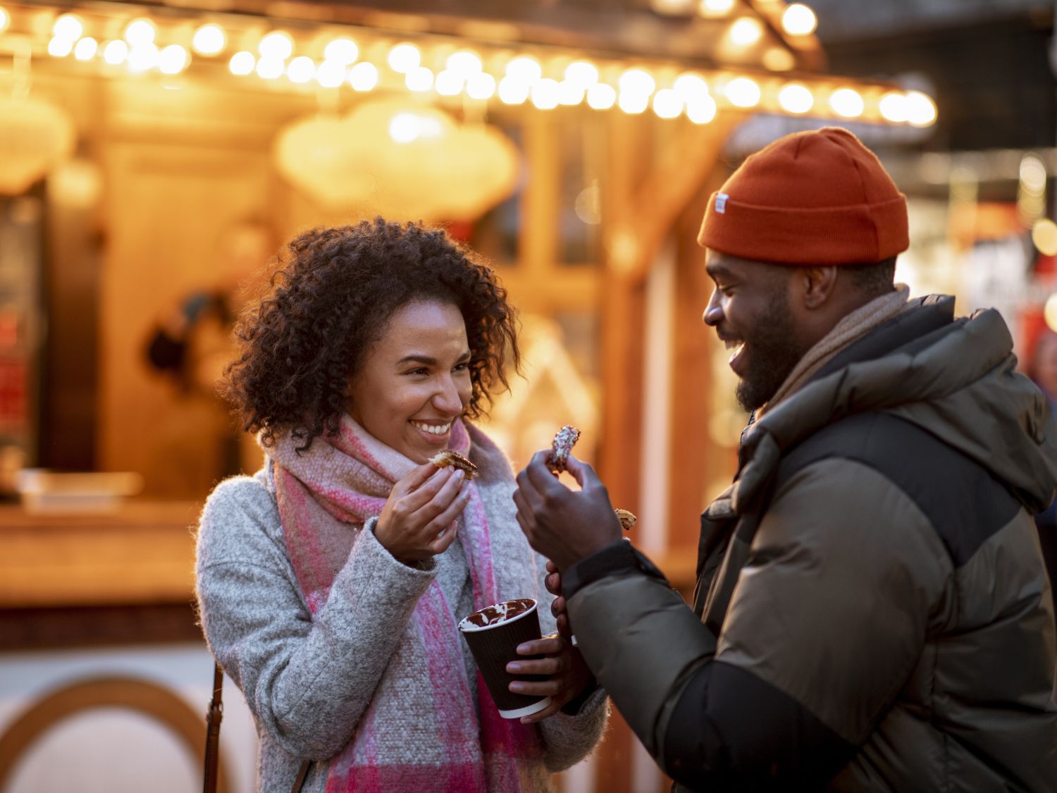 A couple drinking hot chocolate and smiling while standing at a christmas market