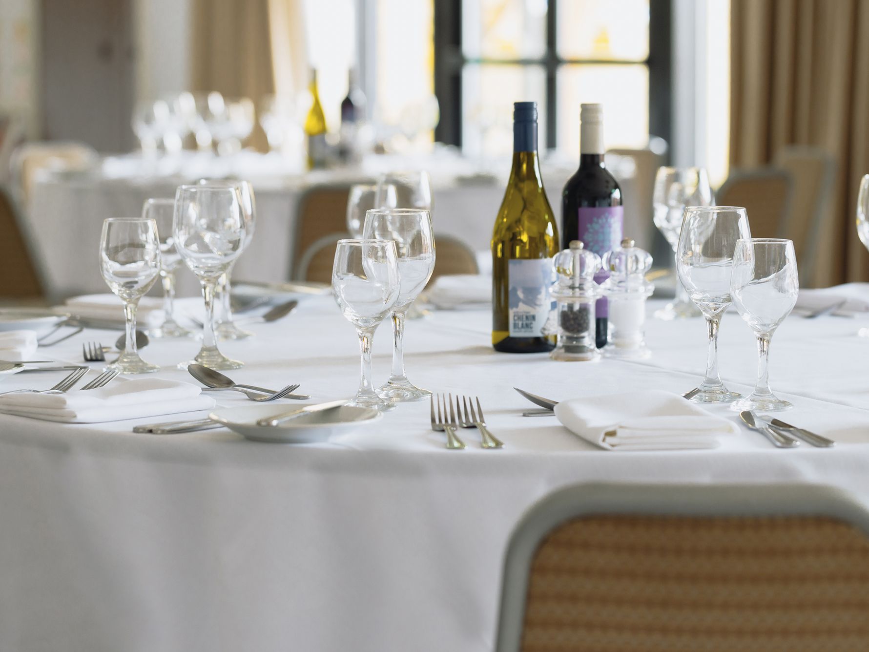 Banquet table with white tablecloths, wine, plate and utensil settings
