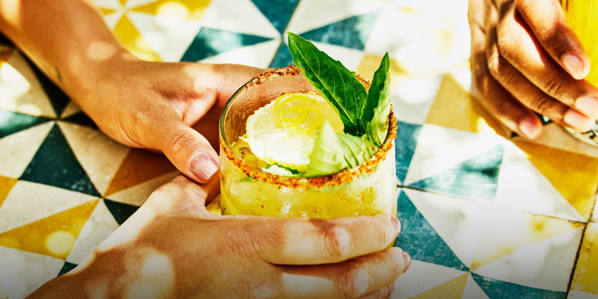 two hands holding colorful cocktails over a brightly tiled table