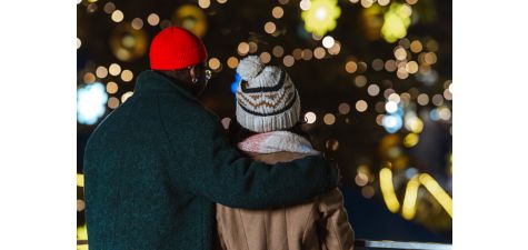 A couple embraces while enjoying the warm glow of festive lights in a winter setting. The intimate scene captures the essence of warmth and togetherness during the holiday season.